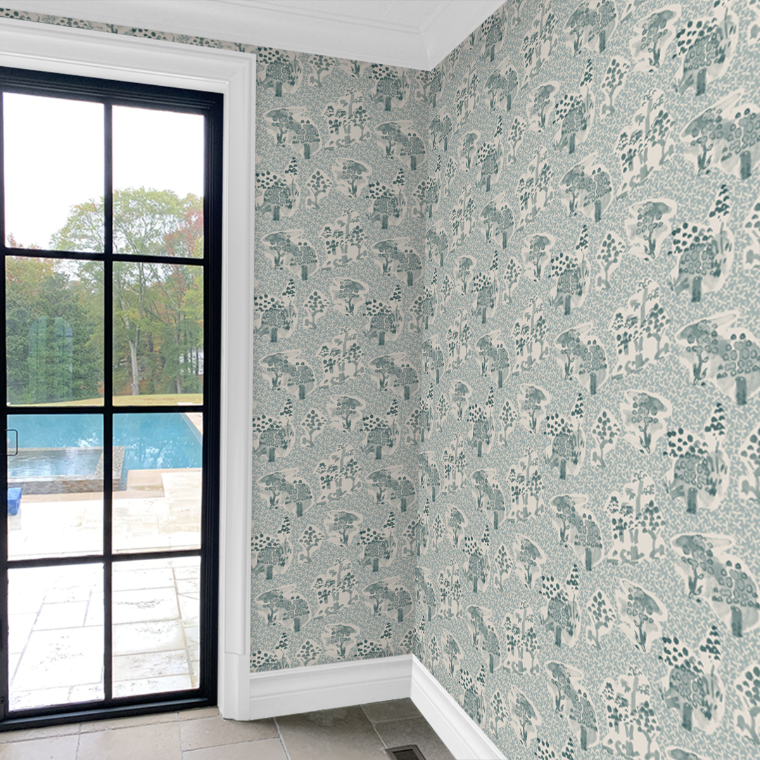 Toile sky blue wallpaper by Angela Simeone installed near a black-framed window, painterly pattern in a real room
